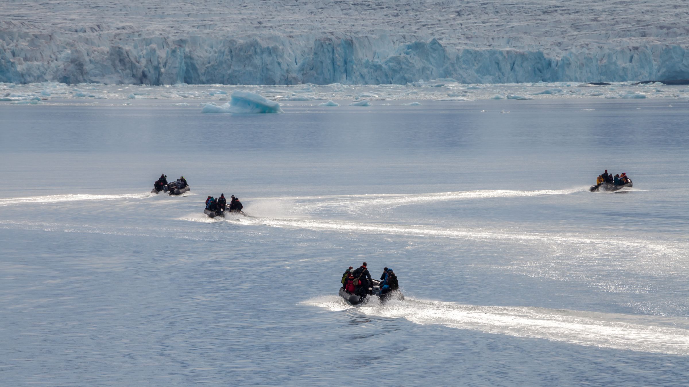 Zodiacs leaving wakes across the still water of Liefdefjord in Svalbard, heading toward the Monaco glacier front